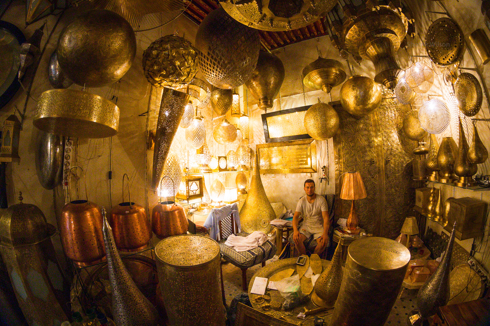 Intricate brass lamps in a lamp shop, with a man sitting in the back