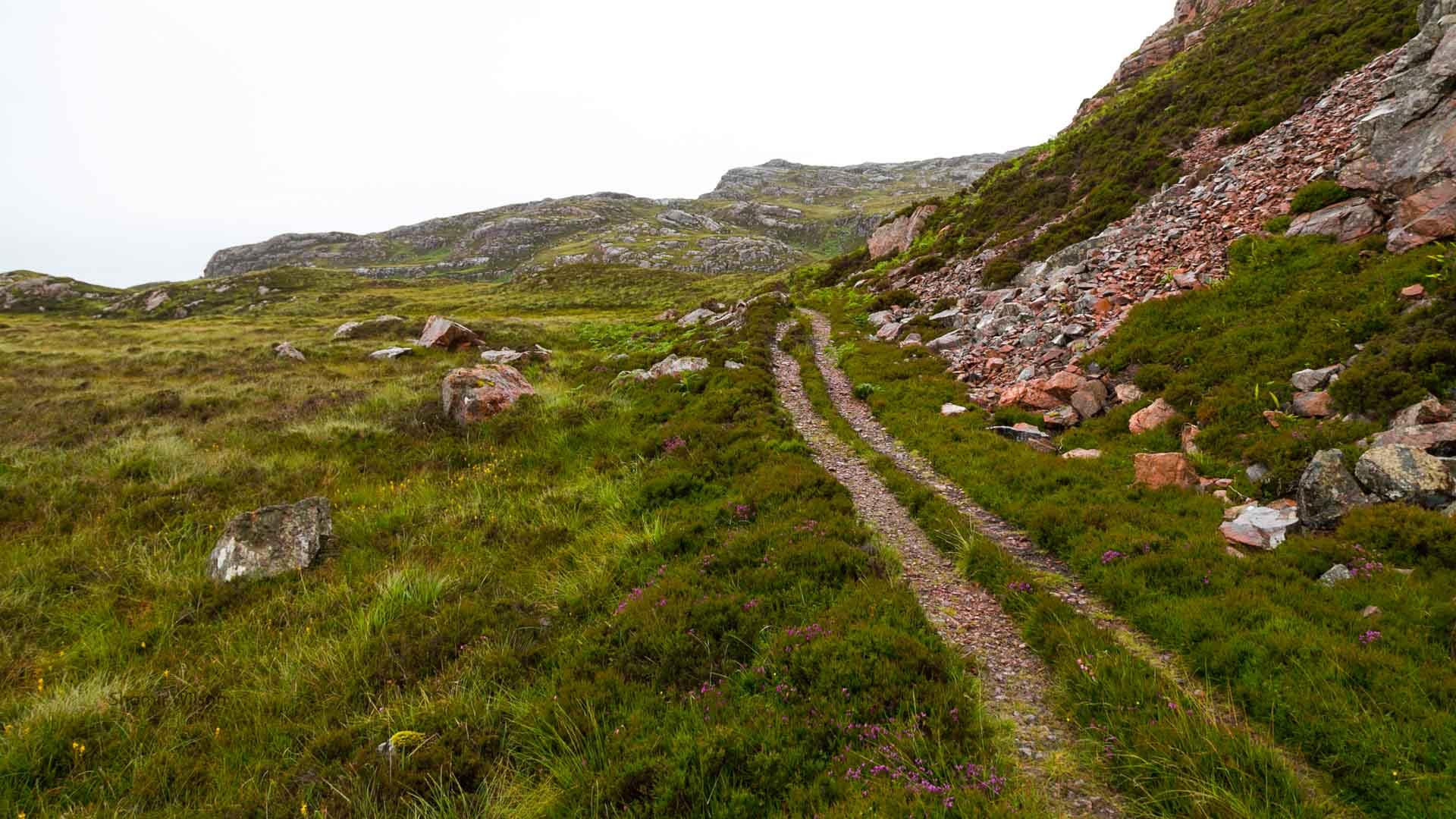 an unpaved tire-track road, uphill across moorish, rocky terrain