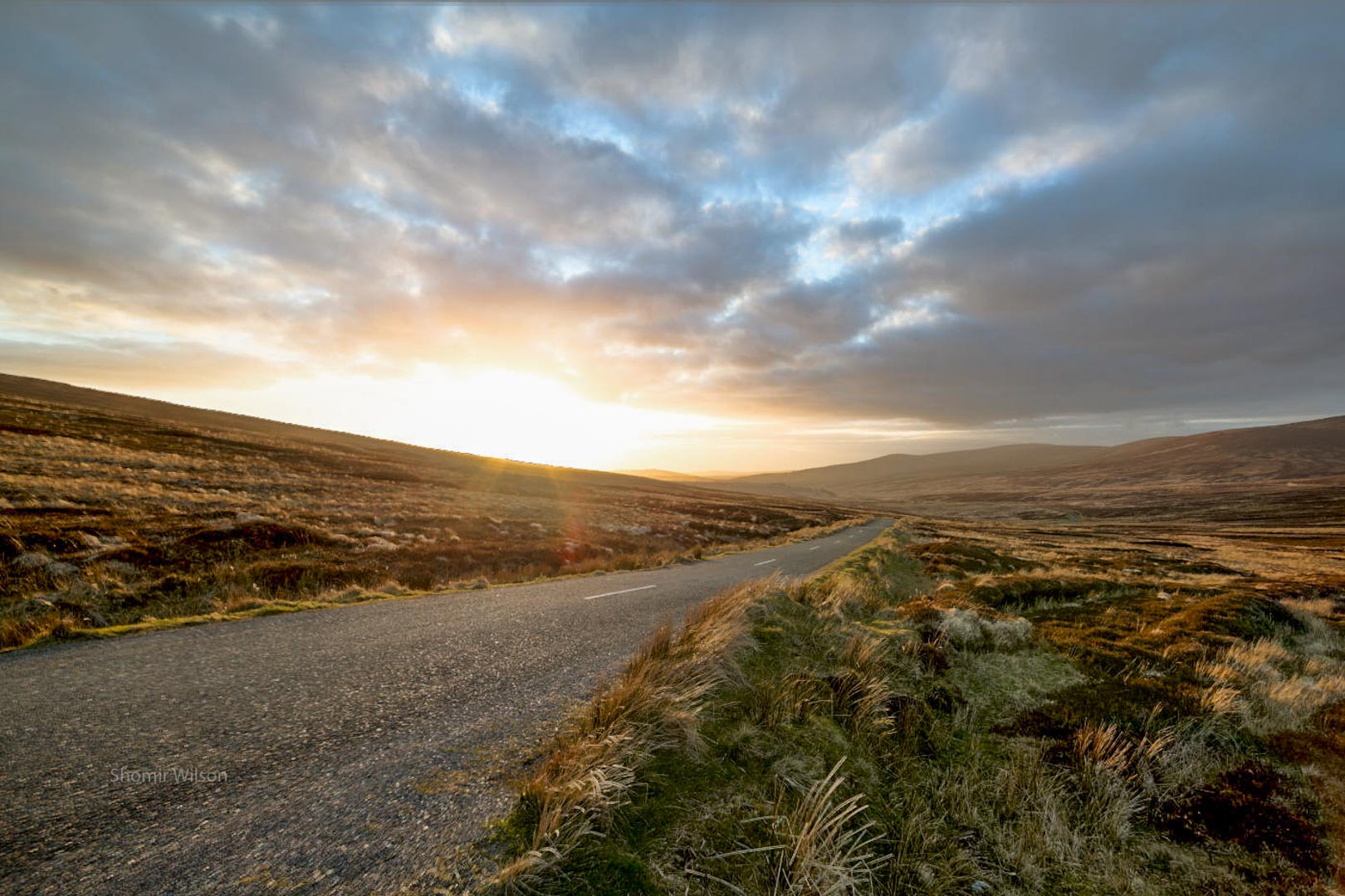 road across a boggy plain with with mountains in the distance and a sunset in the sky