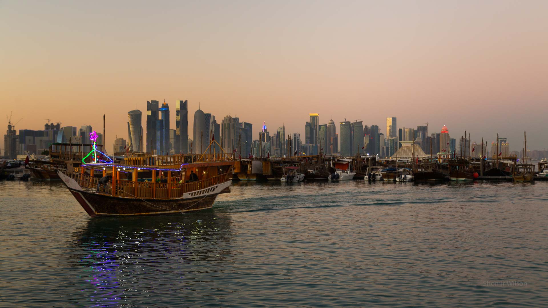 Glittering city skyline at dusk, across a harbor, with boats in the foreground