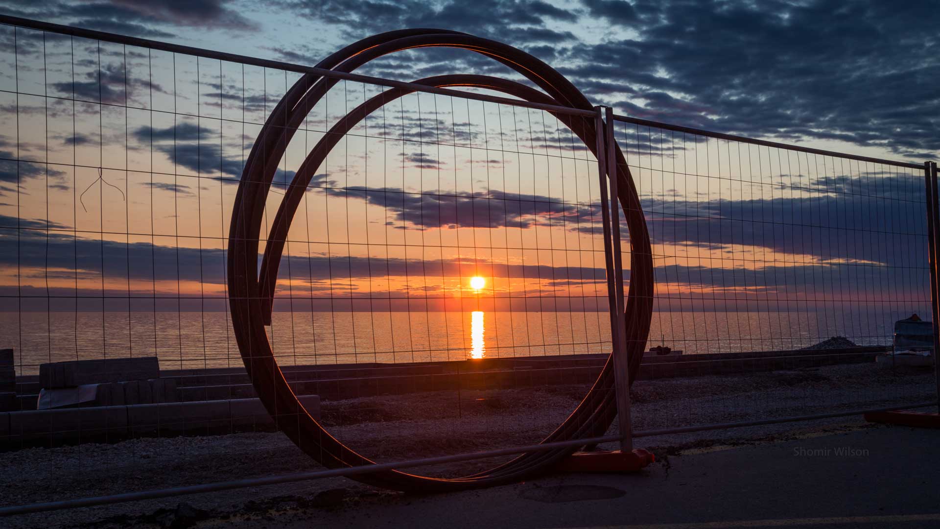 loop of tubing leaning against a fence and encircling a sunset over water