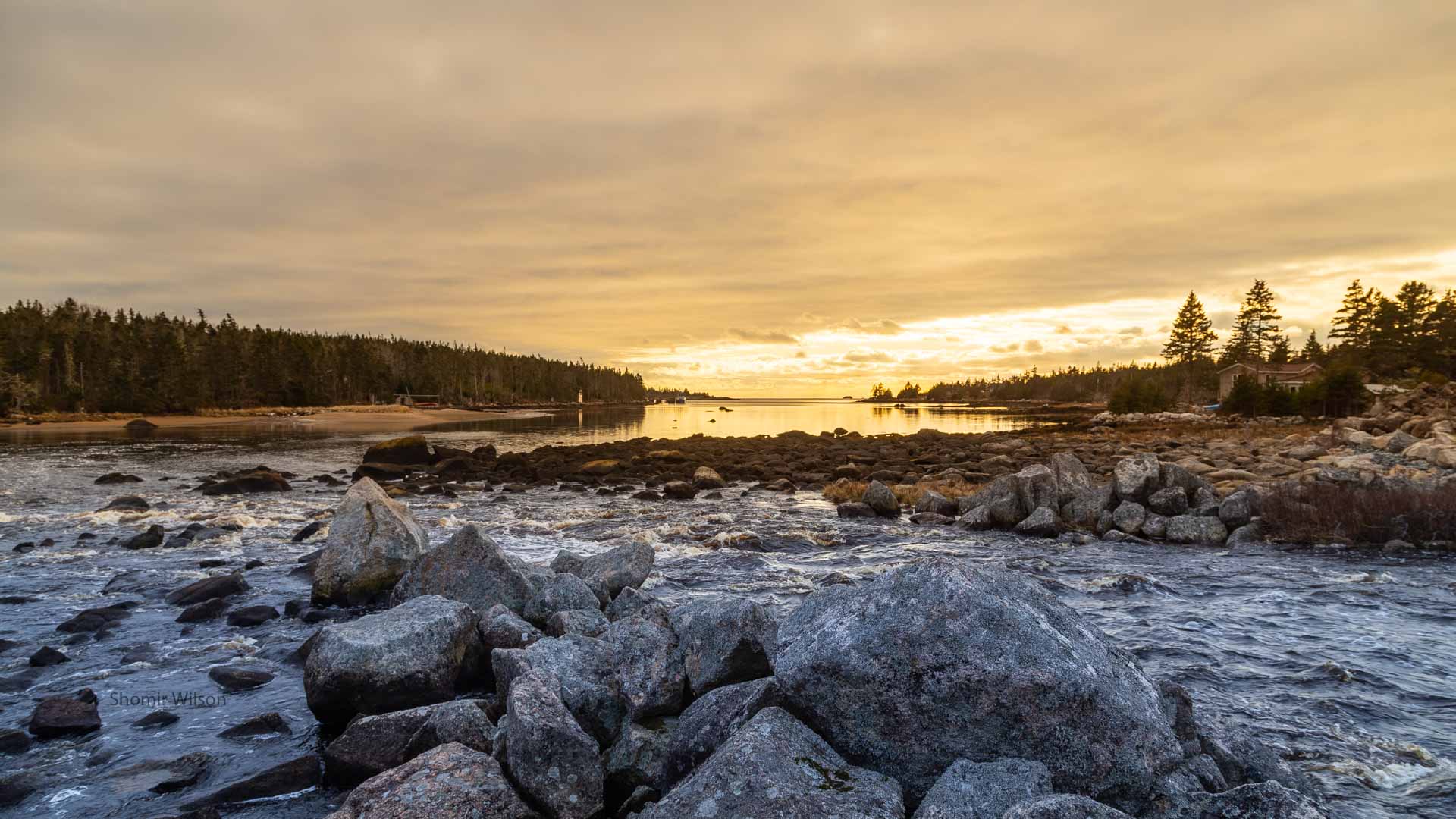 water tumbling over rocks into a small rural bay surrounded by pine trees