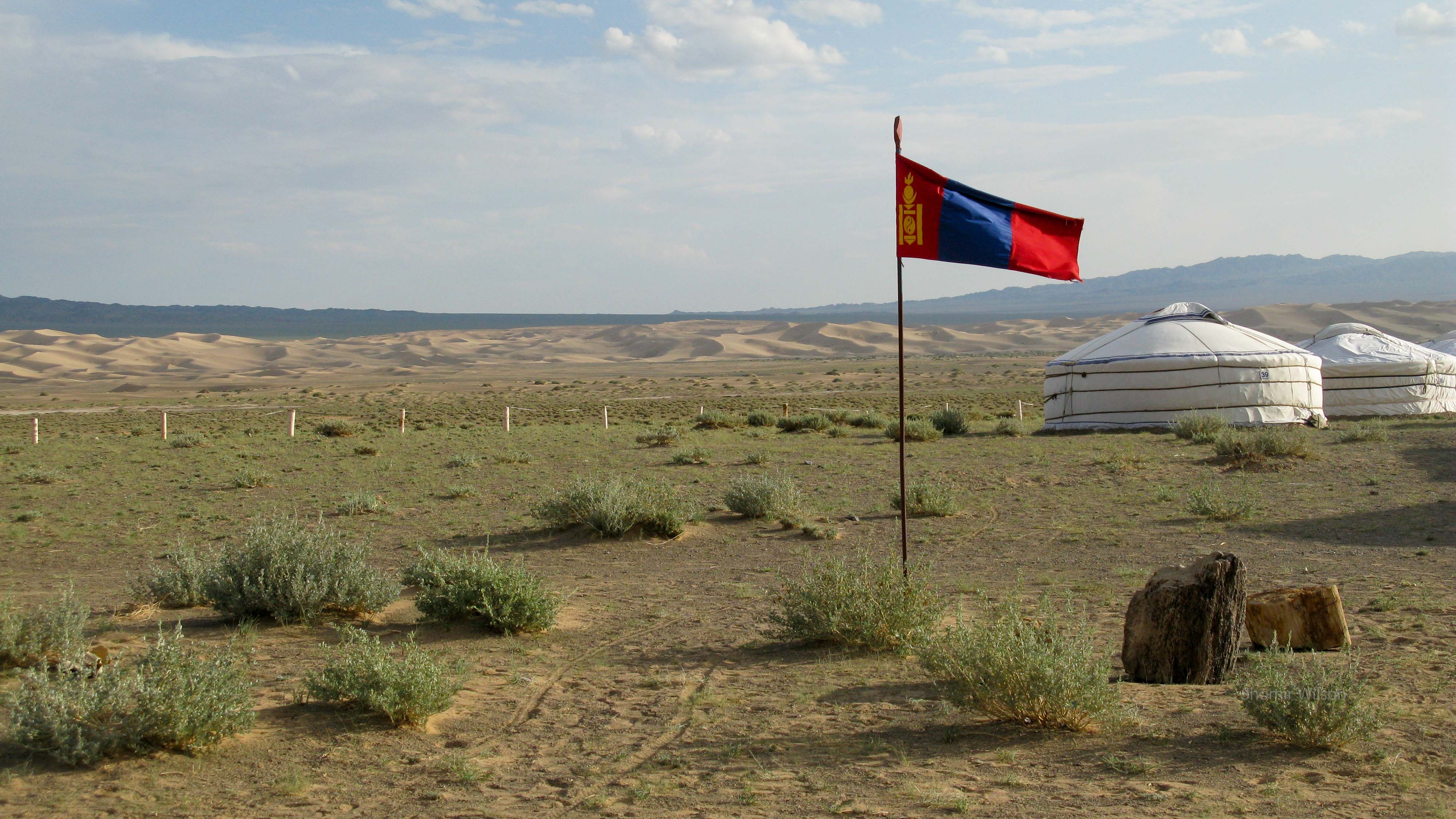Mongolian flag with gers to the left and distant sand dunes to the right