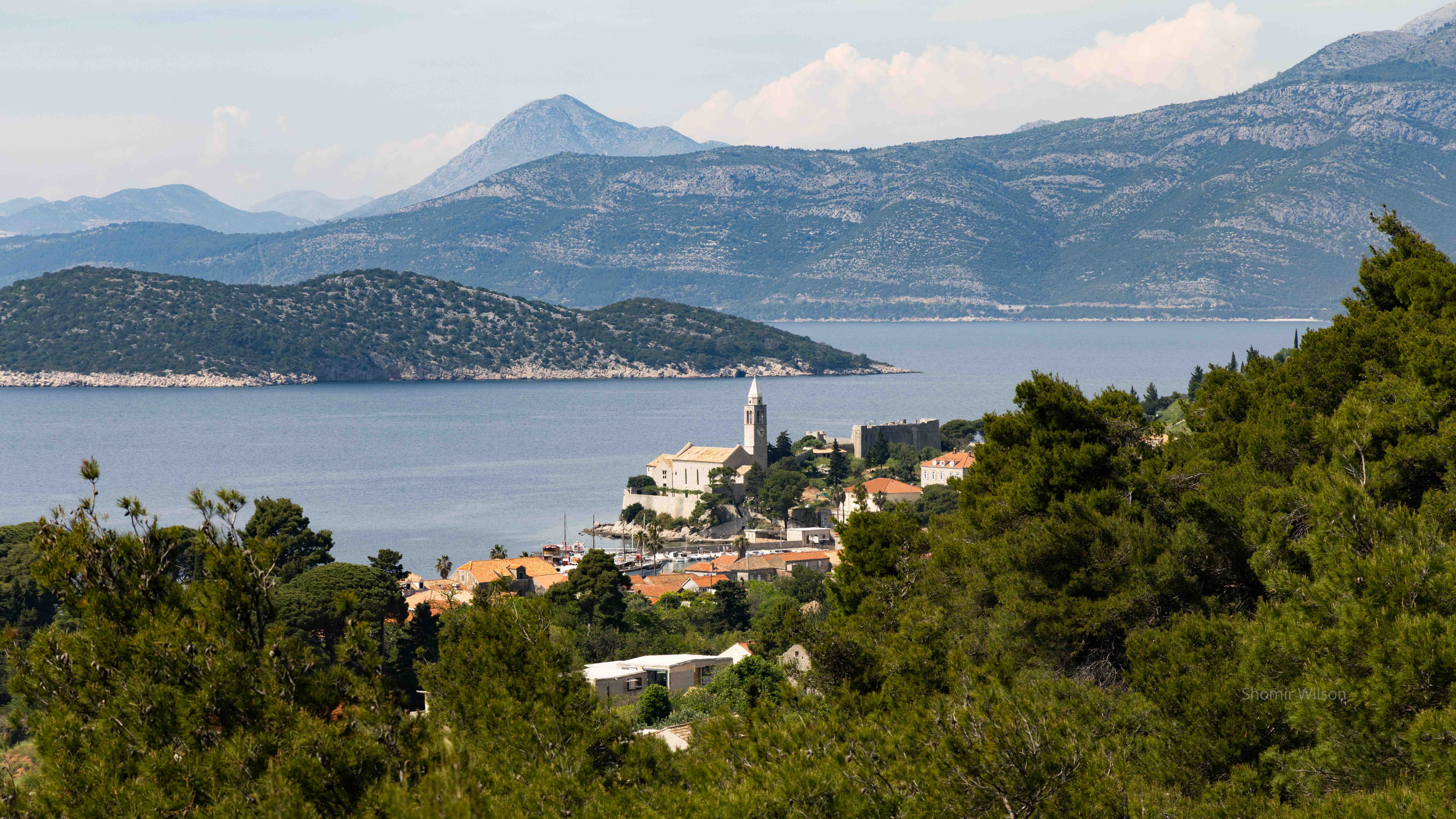 Church and small town on the coast of a small island with other islands in the distance, from a nearby mountain ridge