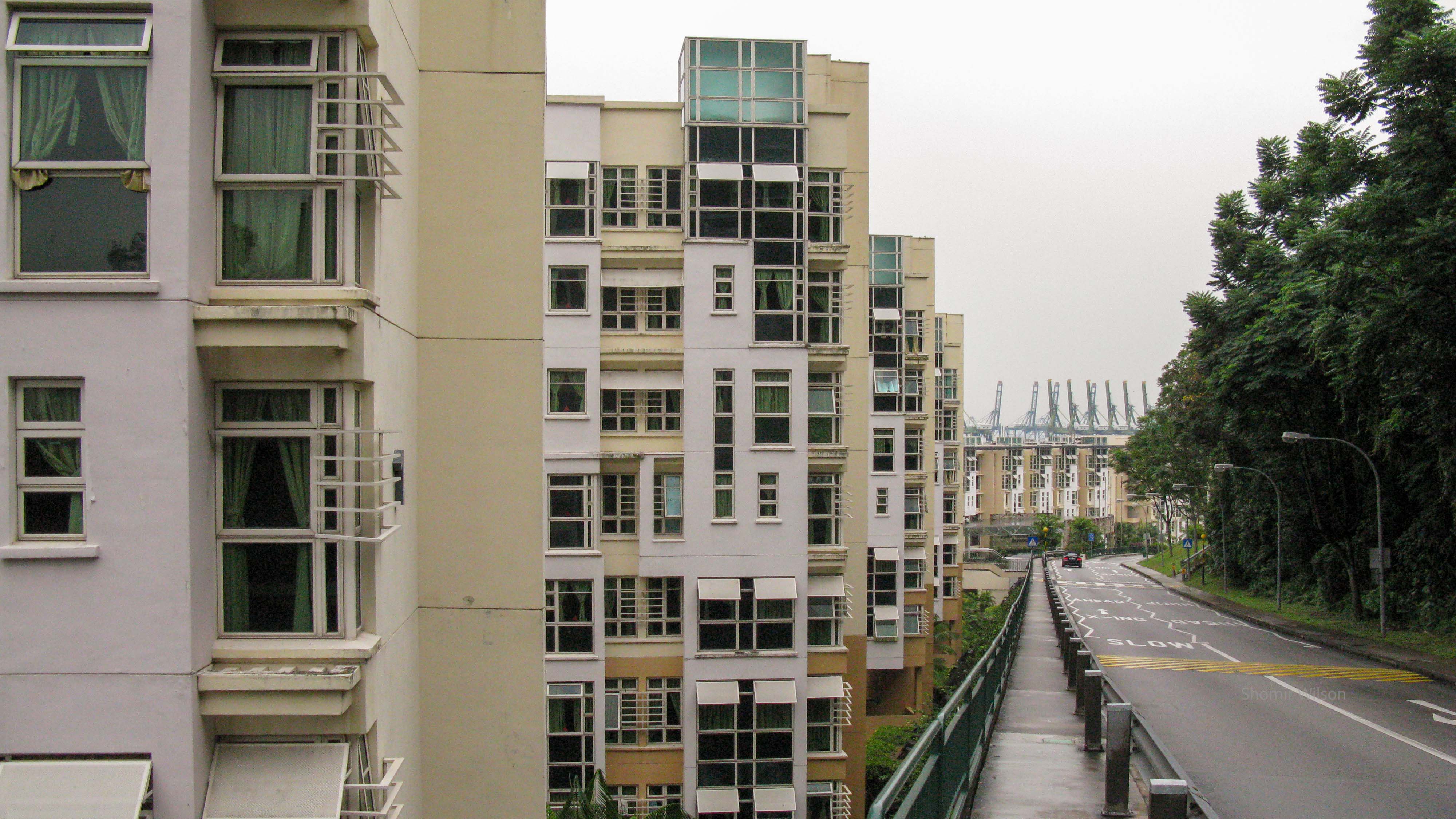 Concrete high-rise dorms next to a road, with a container port in the distance
