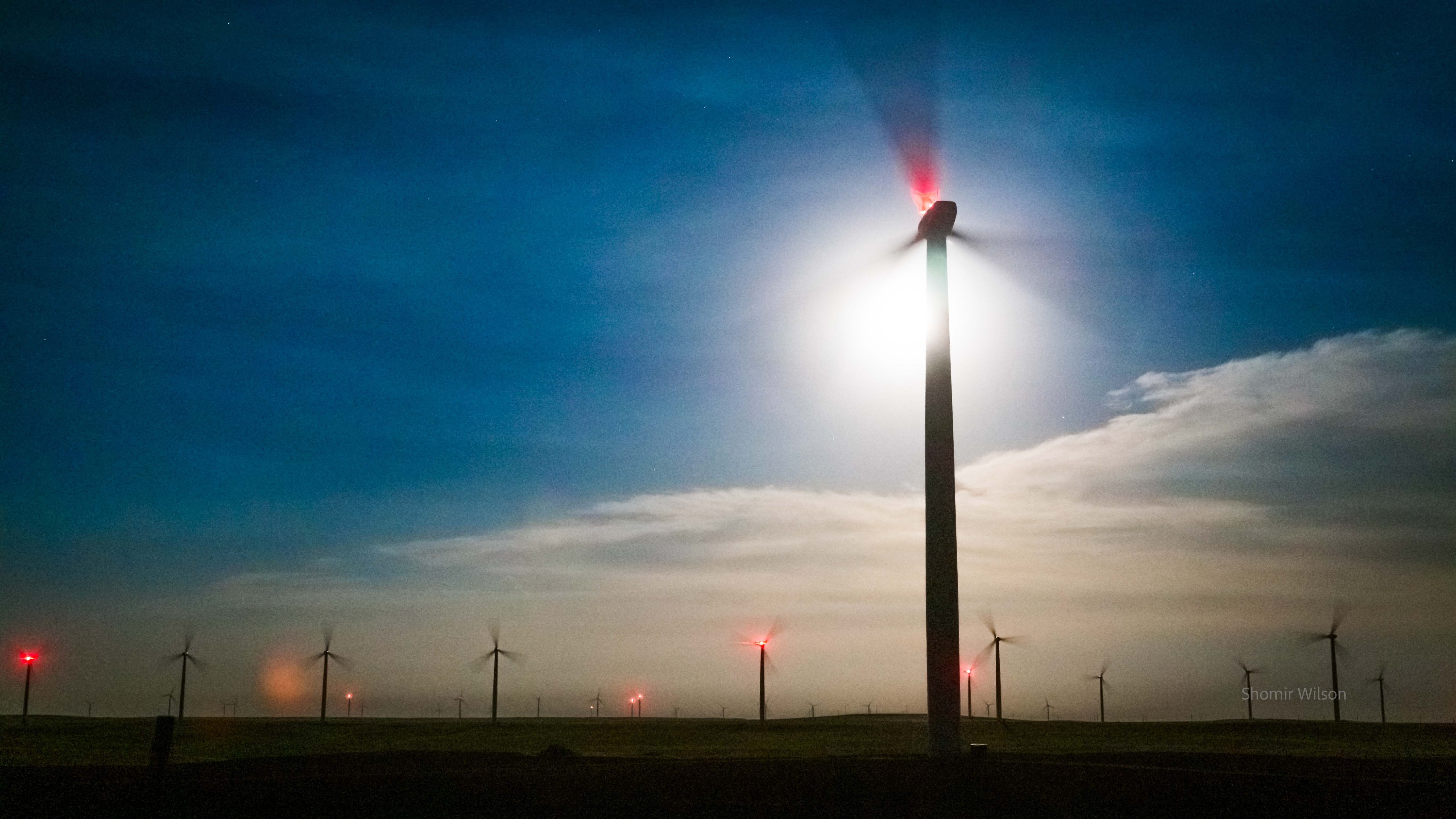 Wind turbines at night, one with the moon overexposed behind it