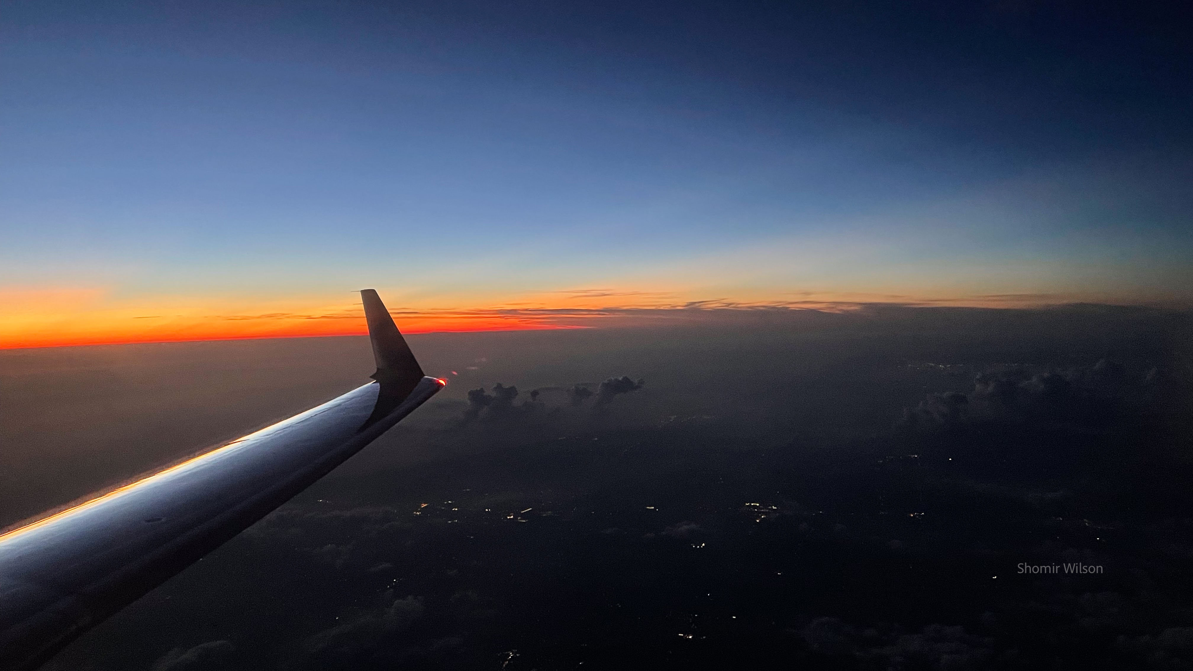 Regional jet wing high above a darkened landscape with a dusky sky