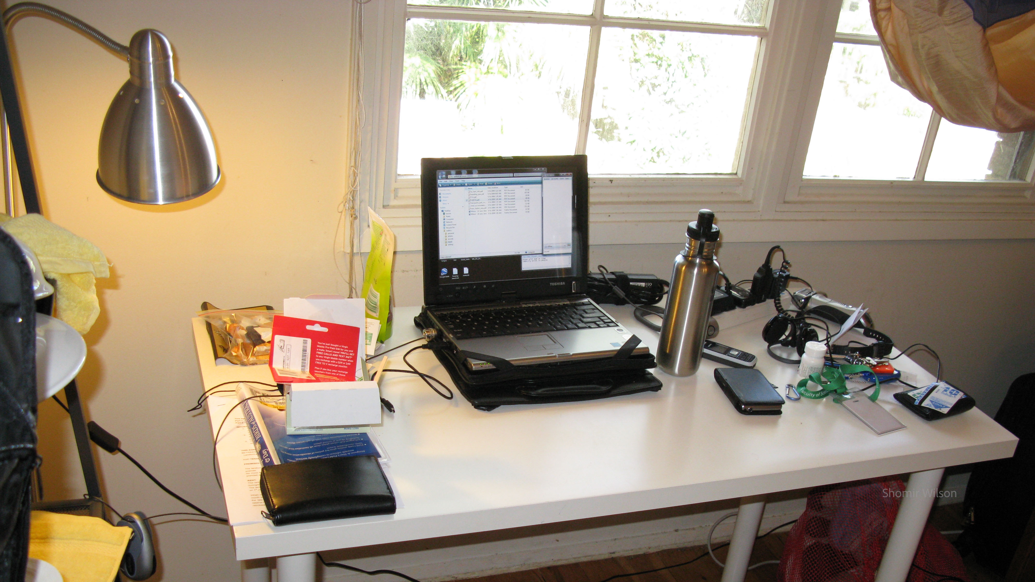 Desk with a laptop in the center and items off to the sides including a candy bar-style mobile phone