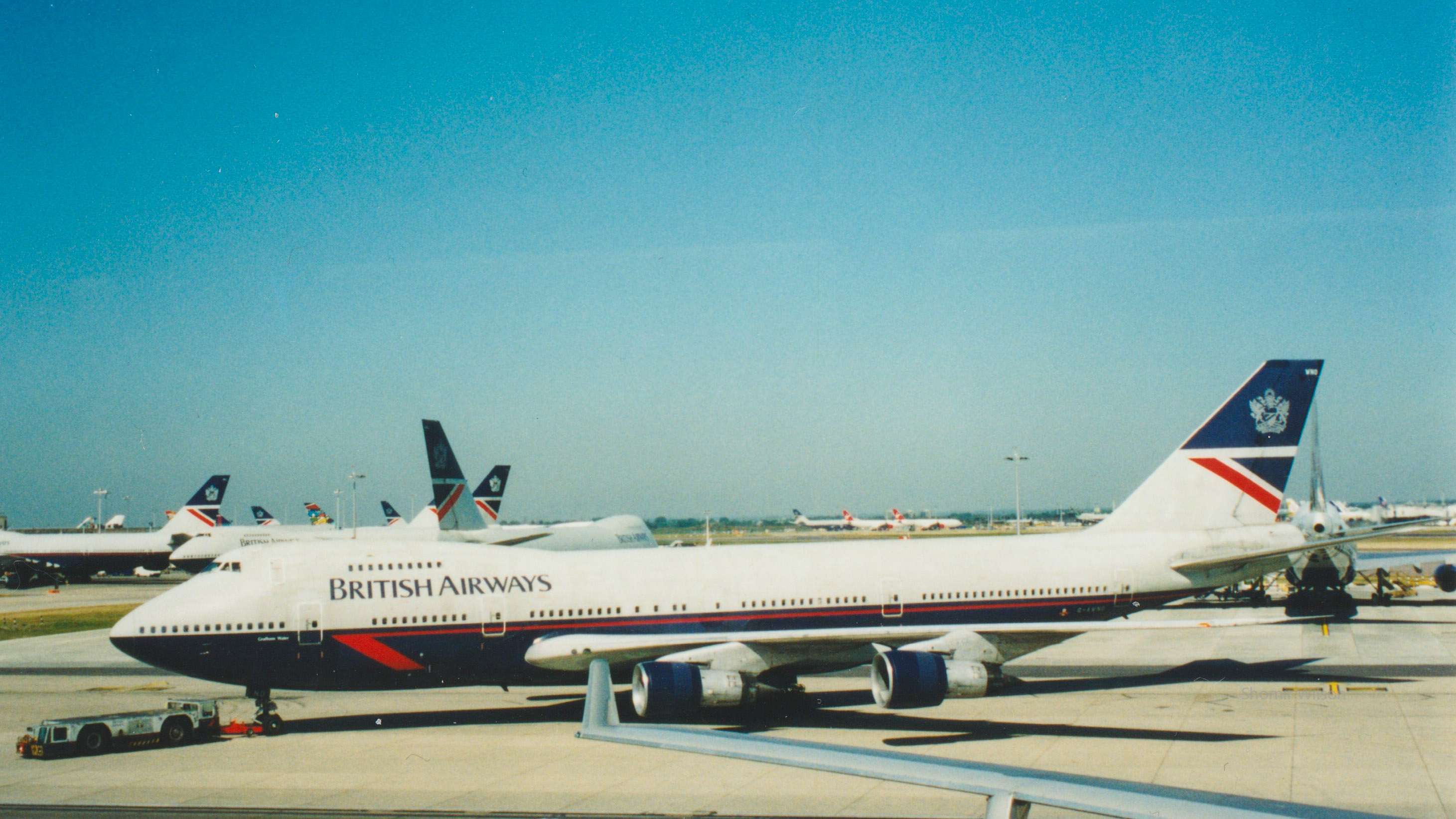Boeing 747-100 in British Airways livery on the apron at an airport, with other British Airways jets in the background