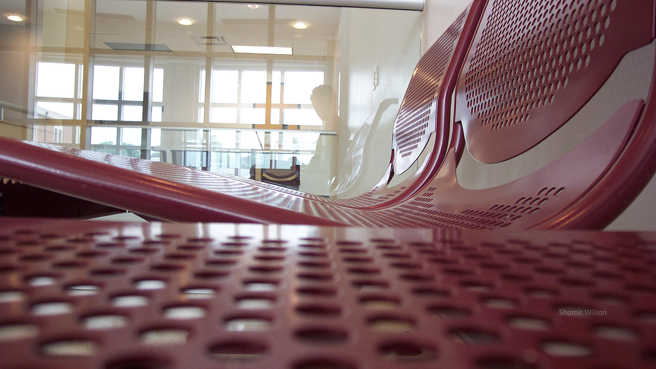 Reflection of me in a large window with a red metal chair around the bottom and right of the frame