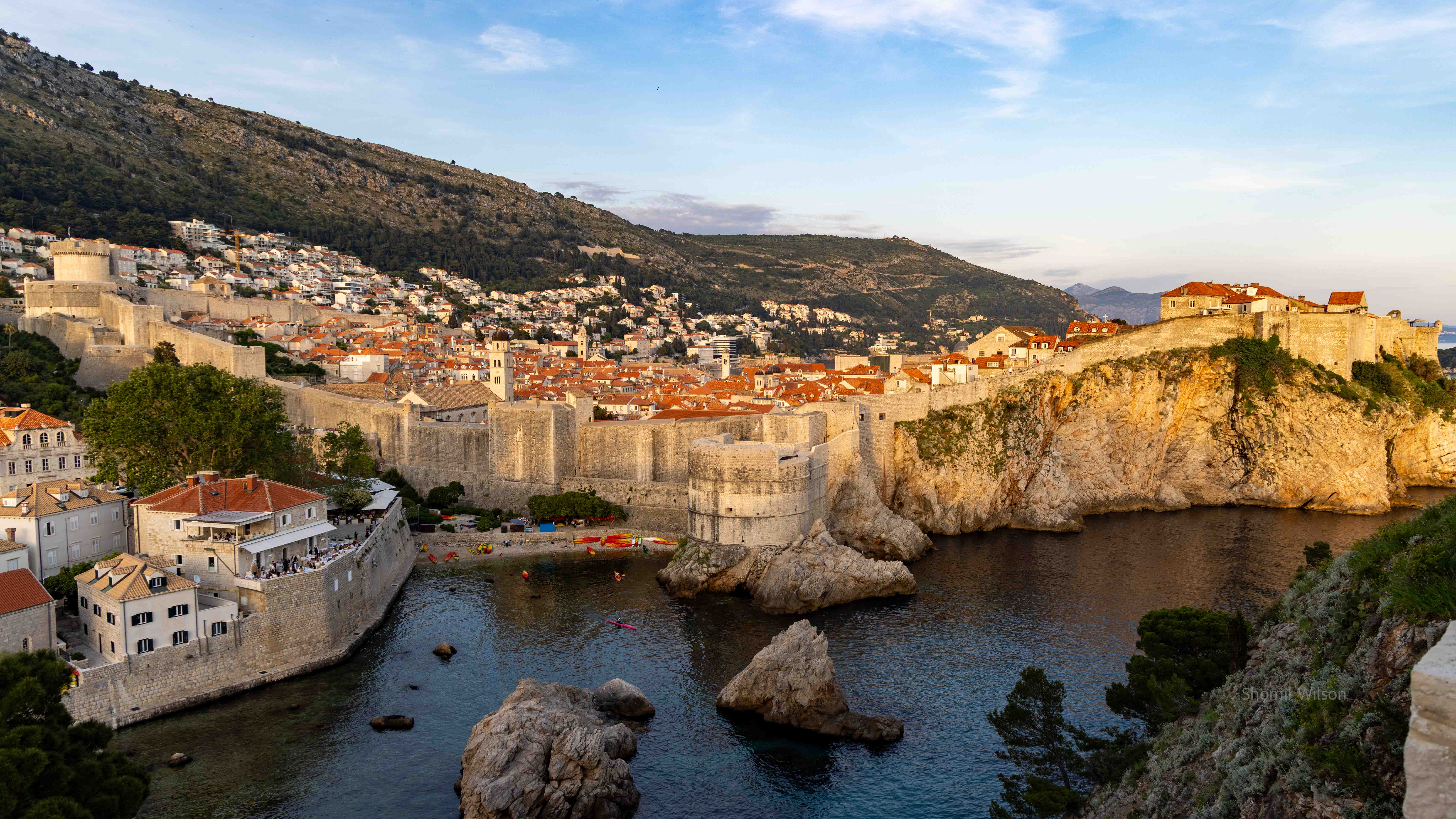Town surrounded by tall wall with a sea inlet in the foreground and hills beyond