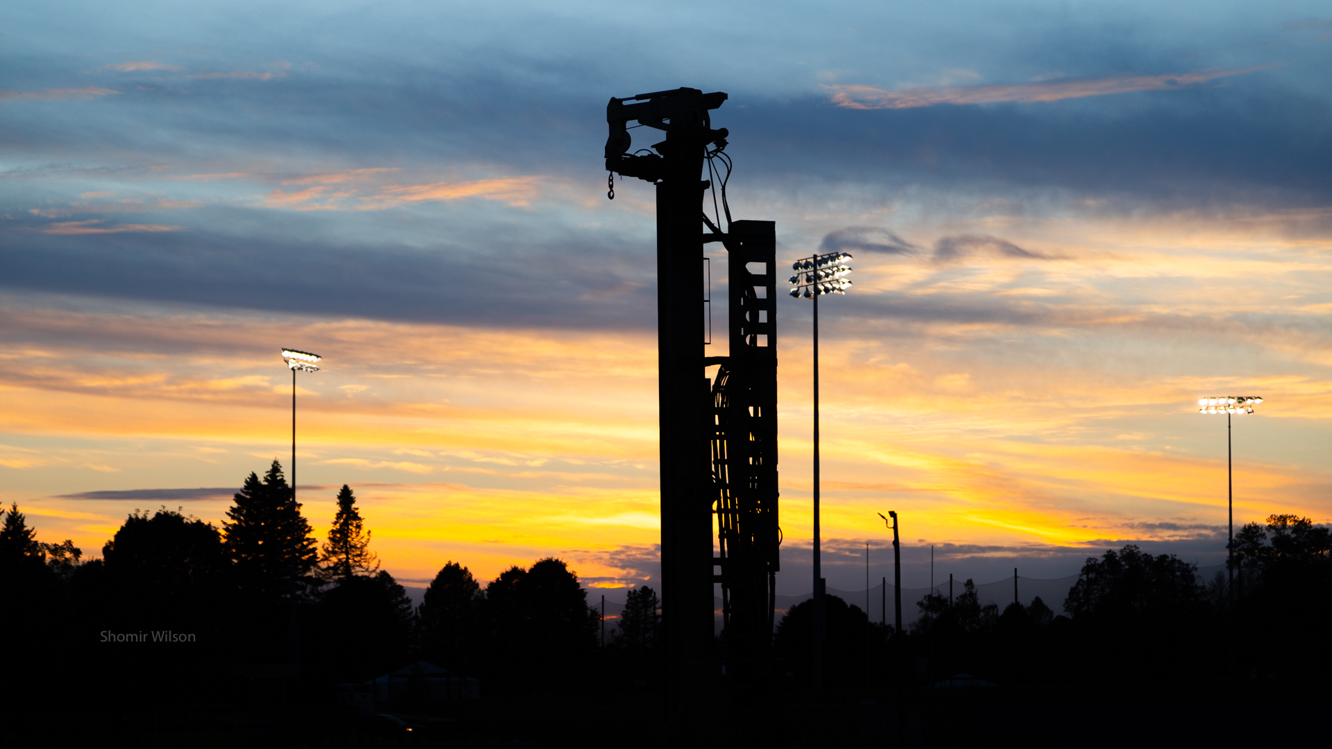 silhouette of a tall pile driver and trees against a sunset in the background