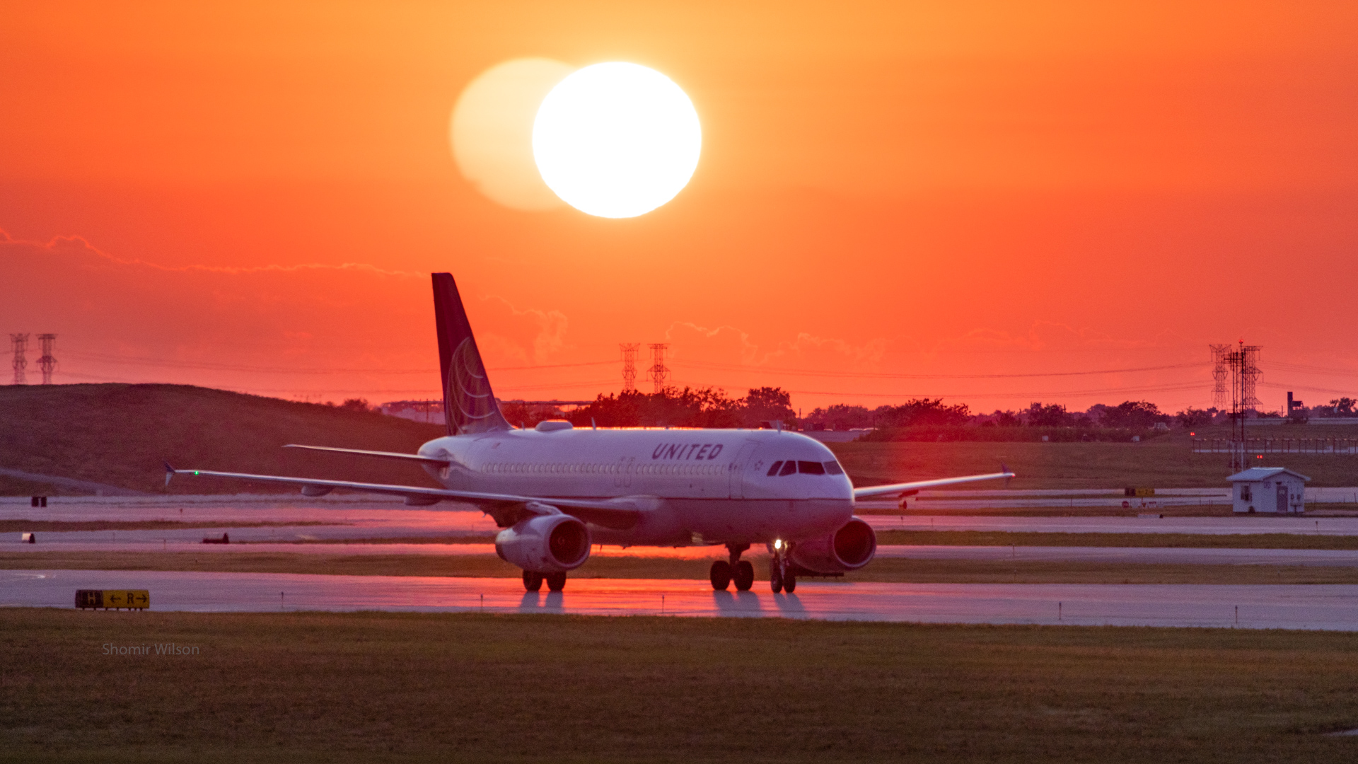 United passenger jet on a runway with a brilliant red sun and sunset above